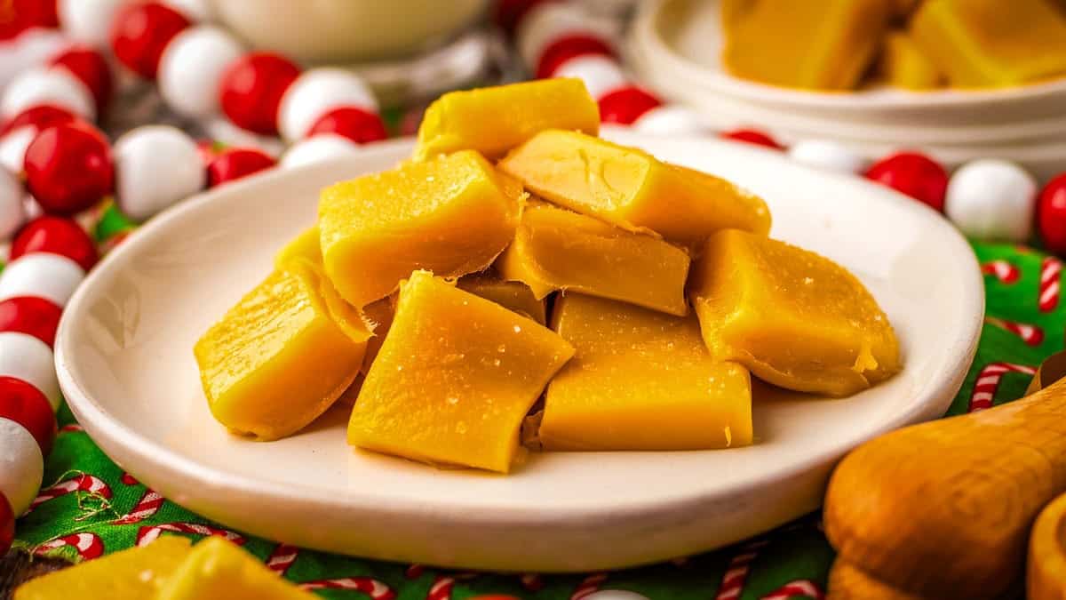 Plate of yellow caramel fudge pieces stacked on a festive tablecloth.