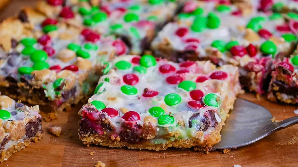 Colorful dessert bars topped with red and green candy-coated chocolates on a wooden surface.