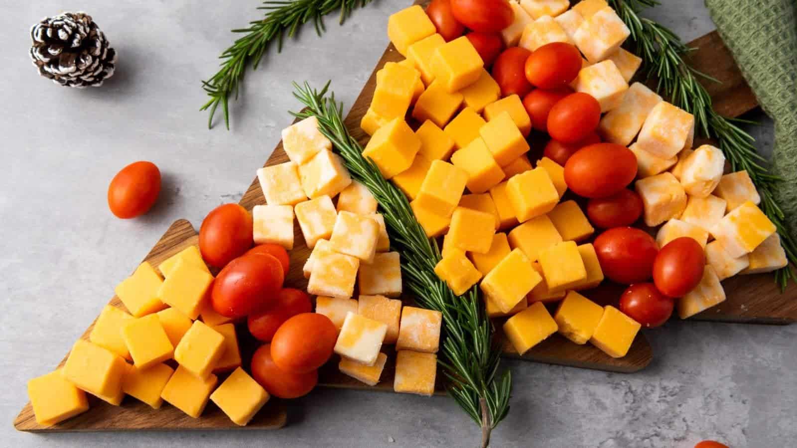 Cheese cubes and cherry tomatoes arranged on a wooden board with rosemary sprigs, resembling a tree.