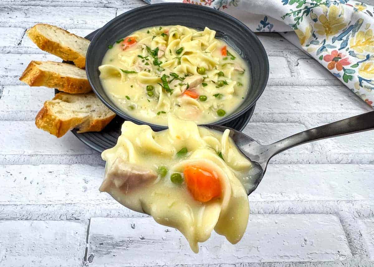 A spoonful of Creamy turkey noodle soup and a bowl in the background.