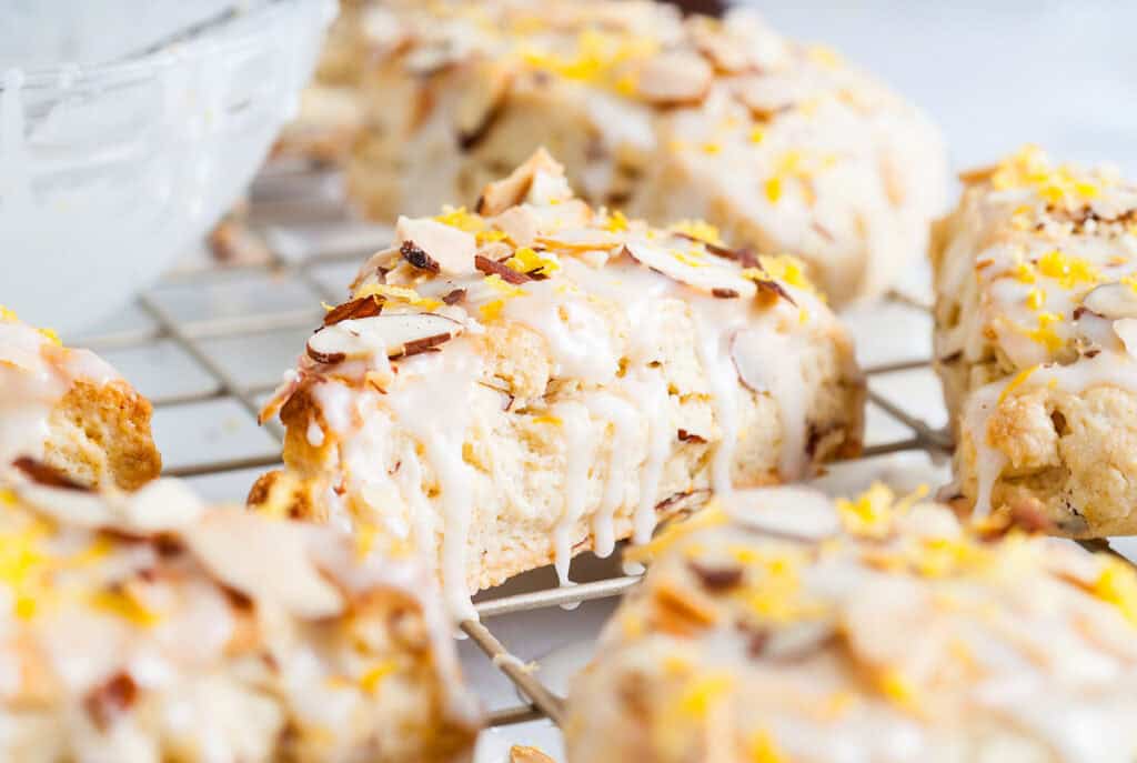 Close-up of delectable glazed scones topped with sliced almonds and lemon zest on a cooling rack, perfect for those exploring new scone recipes.