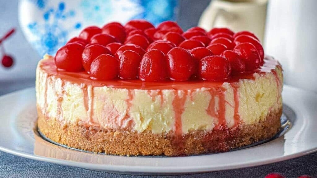 Cherry-topped cheesecake on a white plate, with a graham cracker crust and cherry glaze.