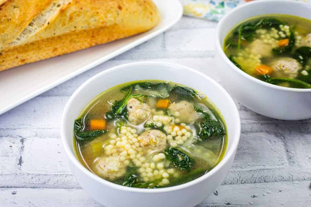 Two bowls of Italian Wedding Soup beside the plate of bread.