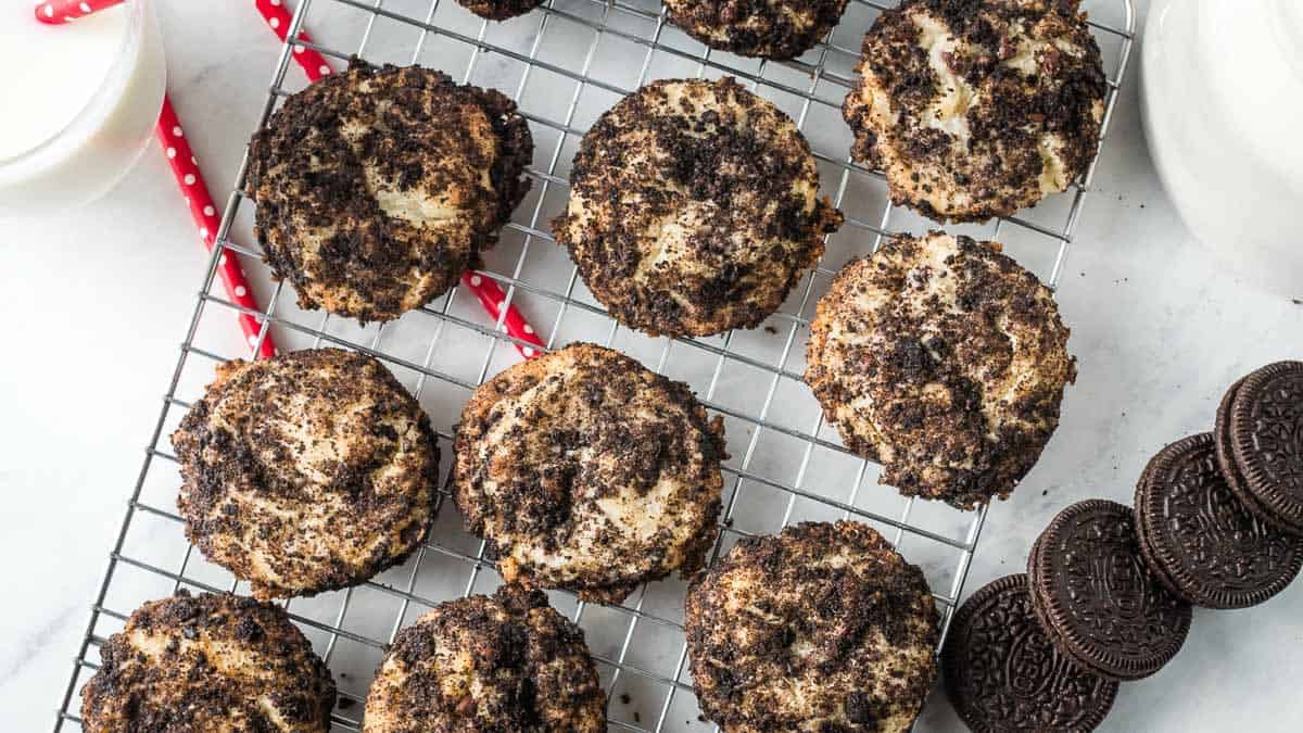 Cookies and cream muffins cooling on a wire rack with Oreo cookies and two red straws in the background.