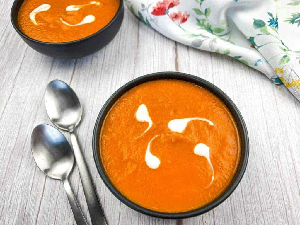 Two bowls of oven-roasted tomato soup with cream swirls.