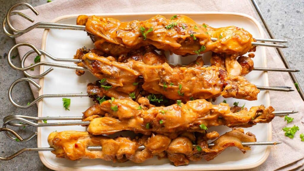 Grilled chicken skewers with a glossy glaze, garnished with chopped herbs, served on a white rectangular plate.