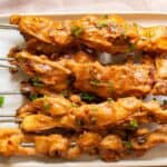 Grilled chicken skewers with a glossy glaze, garnished with chopped herbs, served on a white rectangular plate.