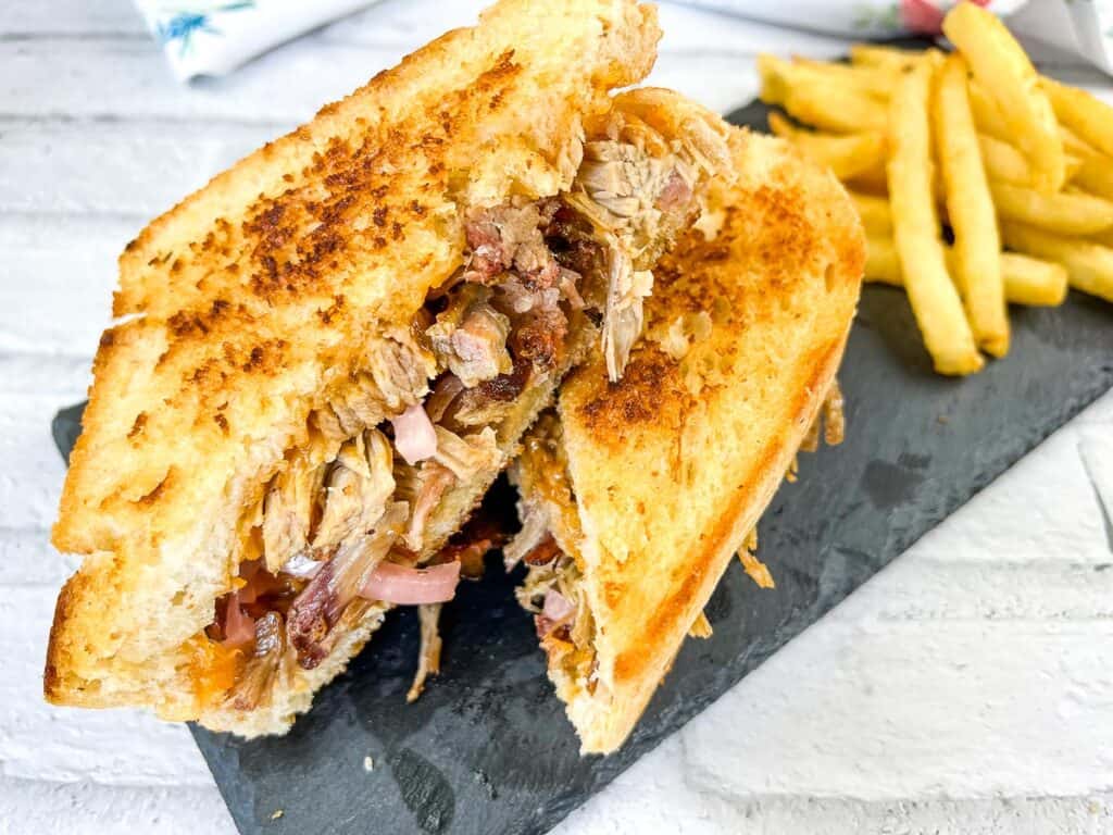 Grilled sandwich filled with pulled pork and onions, served with a side of fries on a slate plate.