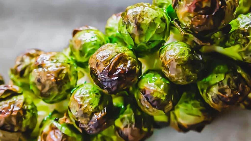 Close-up of roasted Brussels sprouts on a stalk, with charred edges and a glossy appearance.