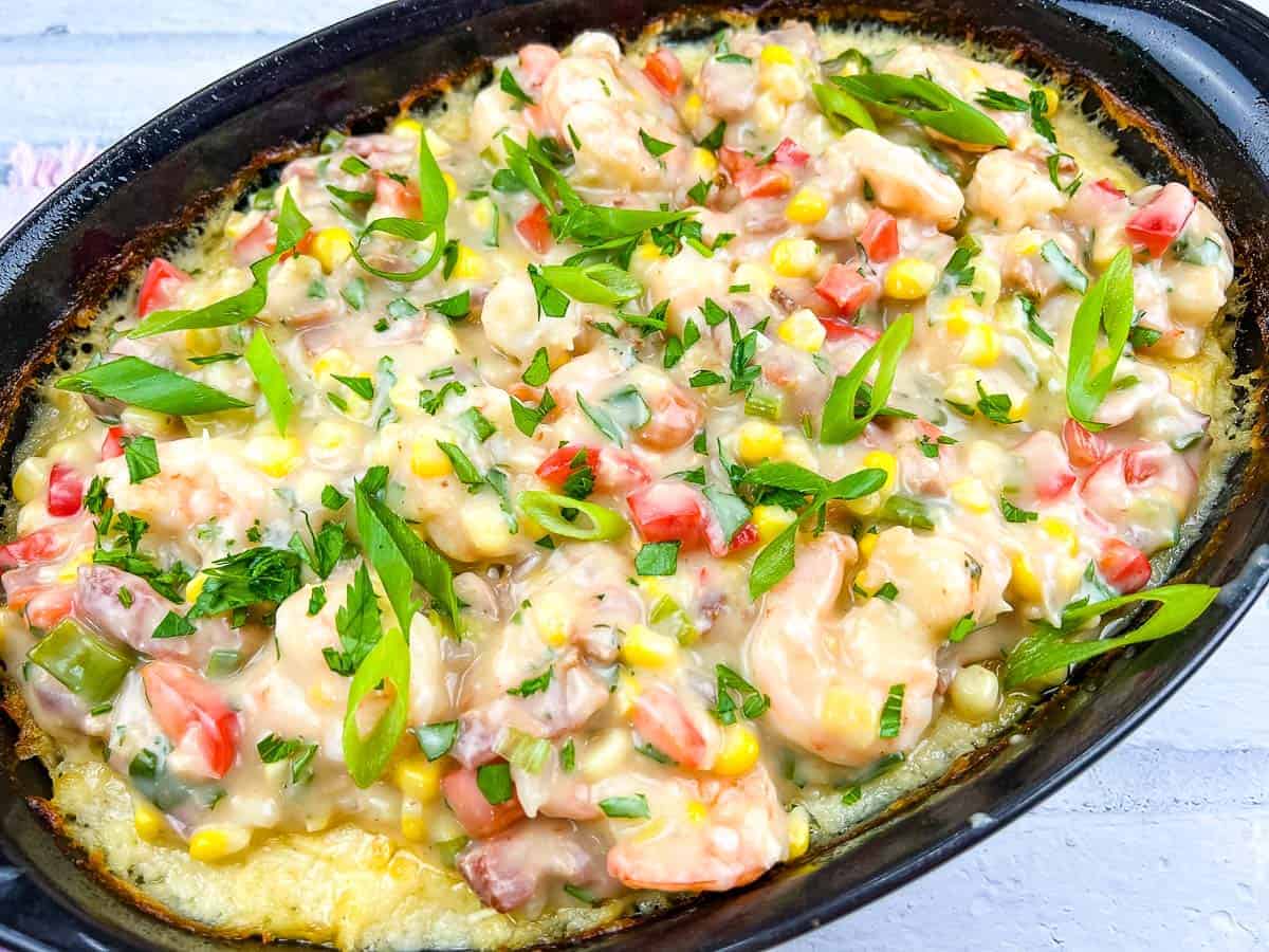 Close-up of shrimp and grits casserole with colorful veggies and spices.