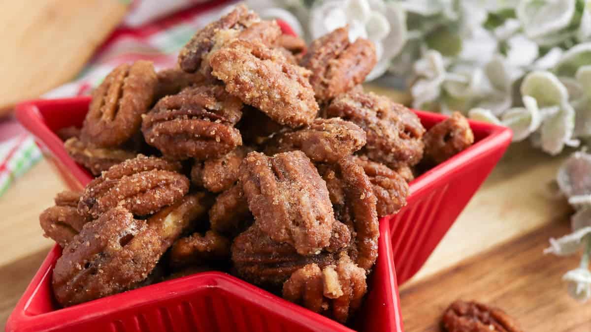 A red, star-shaped bowl filled with candied pecans on a wooden surface.