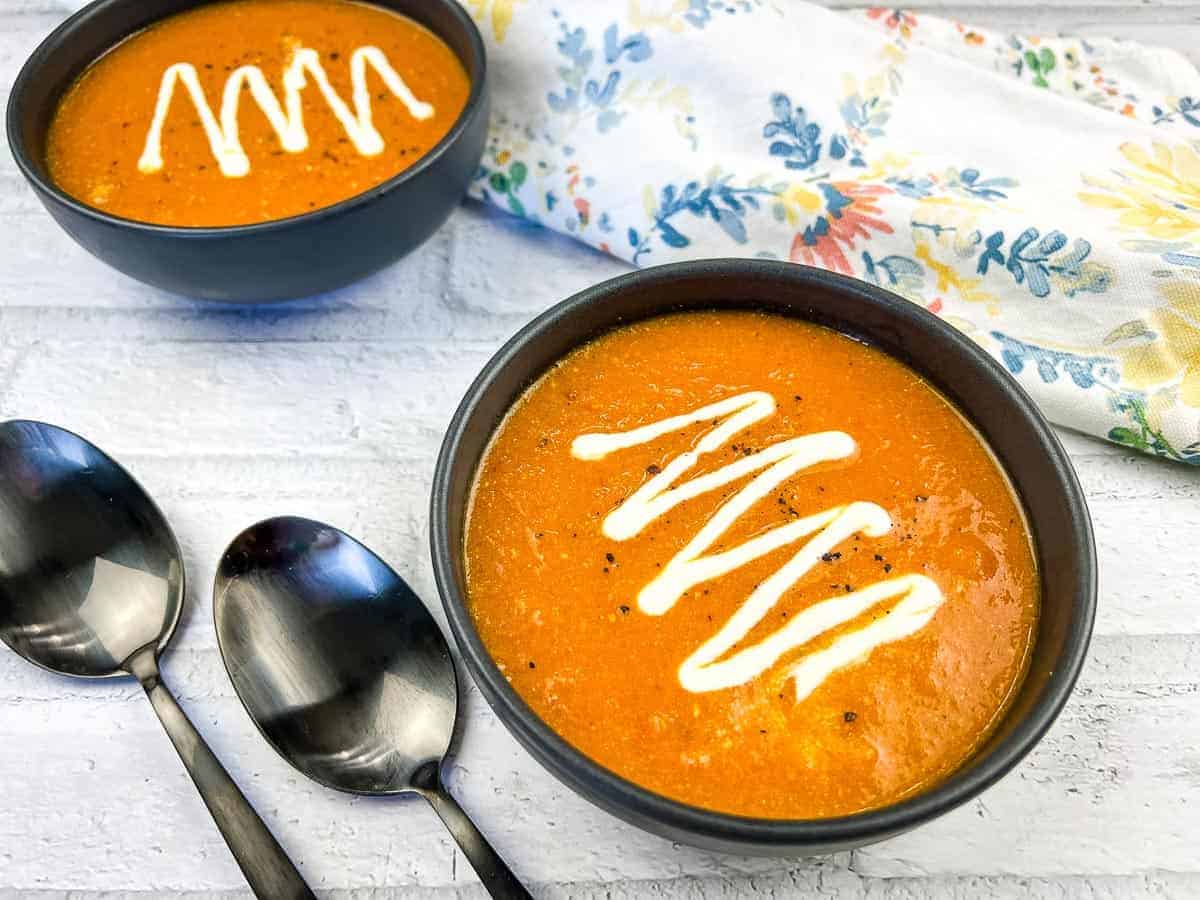 Two bowls of Smoked Tomato Soup with Mascarpone topped with a zigzag of cream.