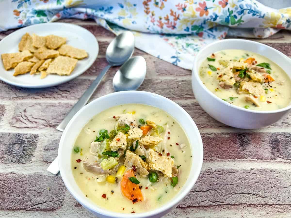 Two bowls of turkey pot pie soup accompanied by two spoons.