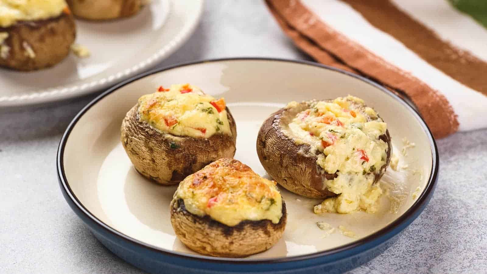 Three stuffed mushrooms topped with melted cheese and diced vegetables on a plate.