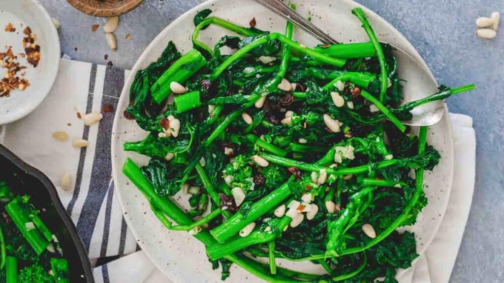 A plate of sautéed greens garnished with pine nuts and raisins, set on a striped cloth with a fork on the side.