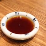 A small white bowl with dark brown Worcestershire sauce placed on a wooden surface.