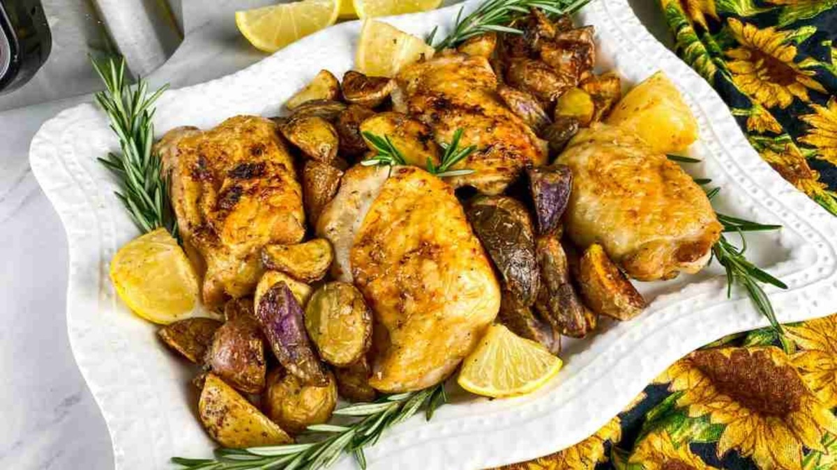 Roasted chicken thighs with potatoes and lemon slices on a white plate, garnished with rosemary sprigs.