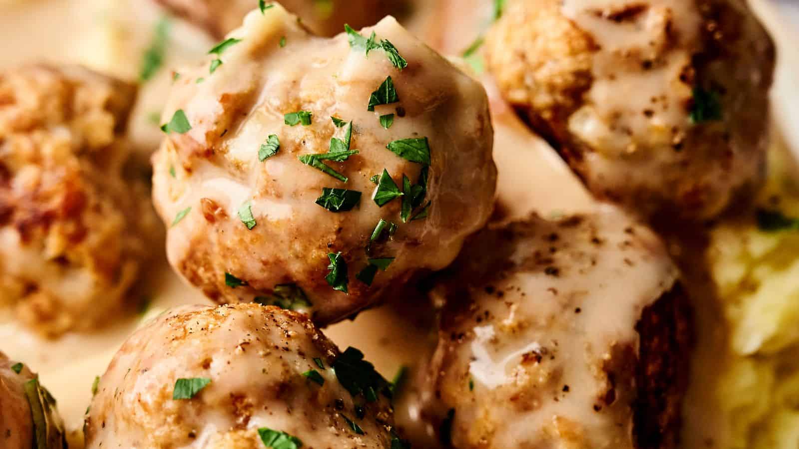 Close-up of meatballs covered in creamy sauce, garnished with chopped parsley.
