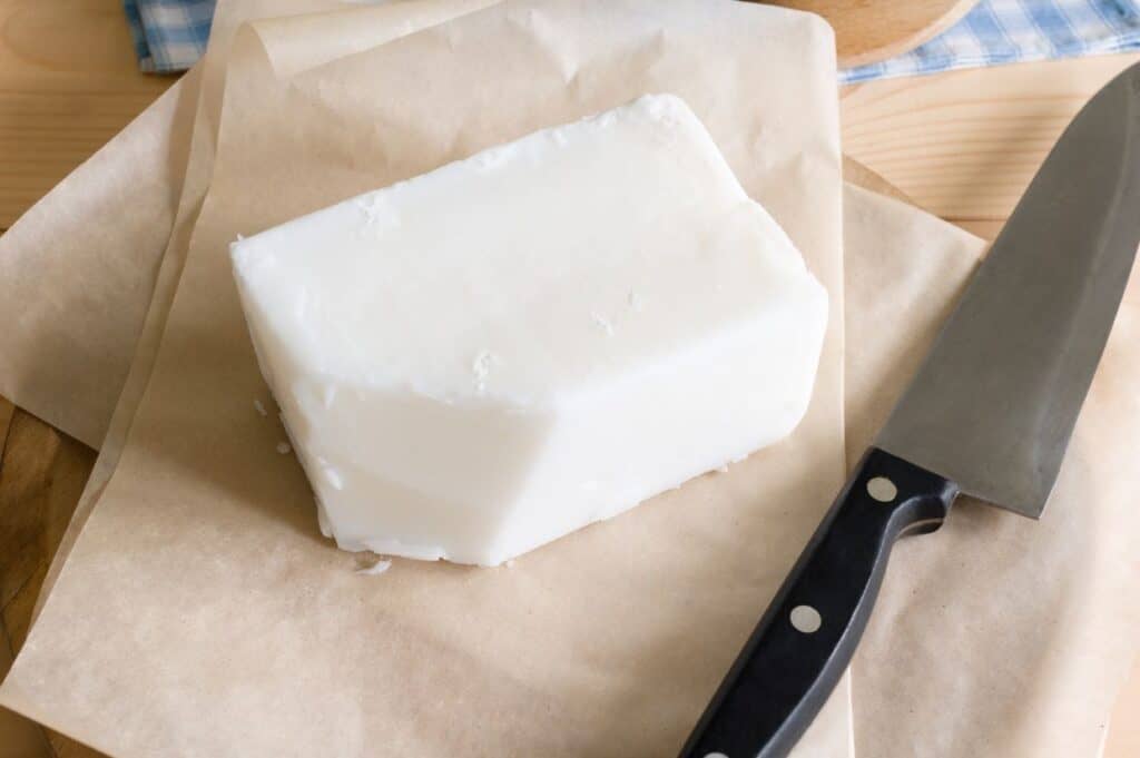 A block of white lard on parchment paper next to a large kitchen knife.