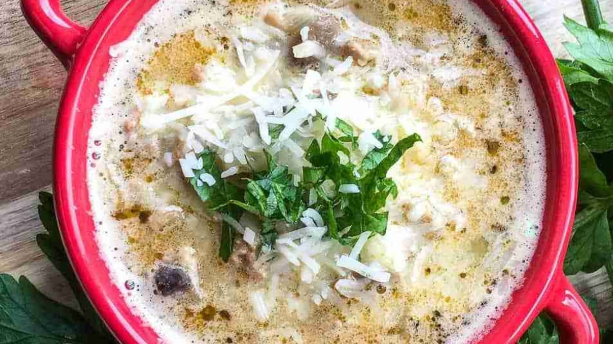 A red bowl filled with creamy mushroom soup, topped with grated cheese and a garnish of parsley.