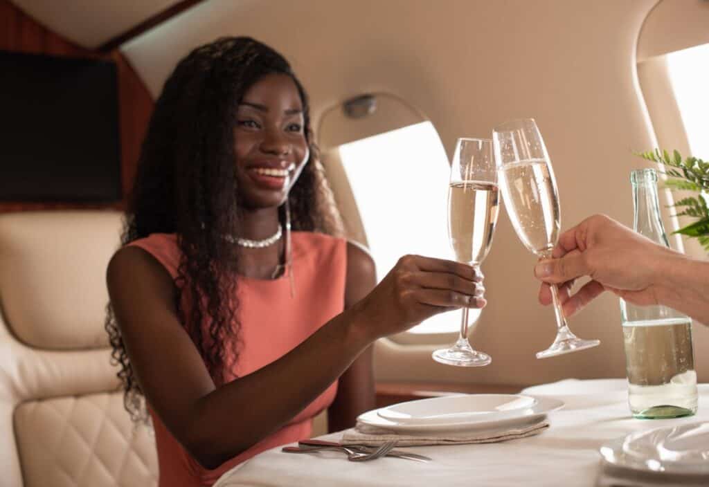 A woman in a pink dress clinks champagne glasses with another person inside a private jet.