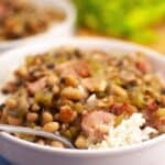 A bowl of Hoppin' John, featuring black-eyed peas, rice, and diced ham, garnished with chopped green onions.