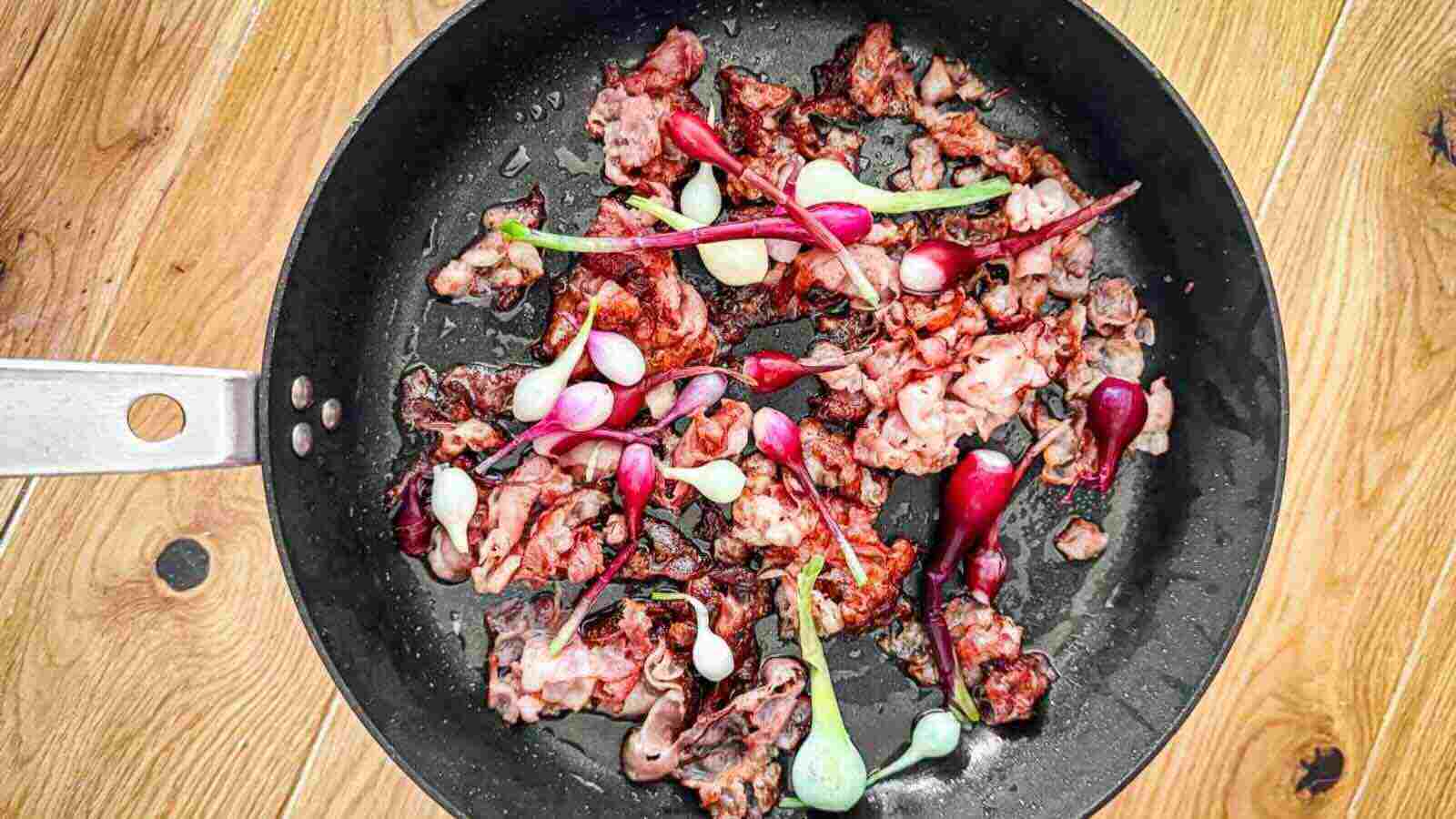 A pan with cooked bacon and raw purple onions.