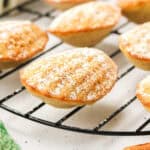 Madeleines dusted with powdered sugar on a cooling rack, next to a green plaid cloth.