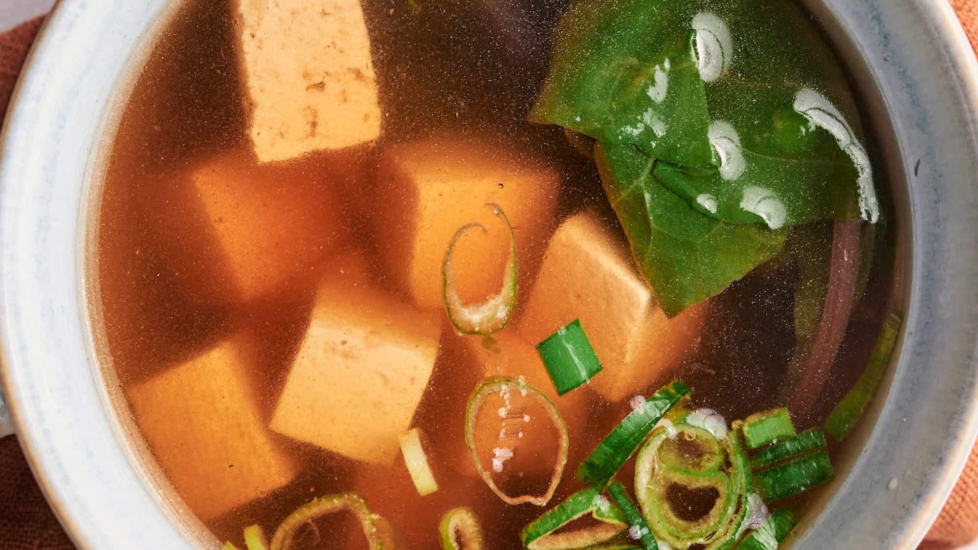 A bowl of miso soup with tofu cubes, seaweed, and green onions.