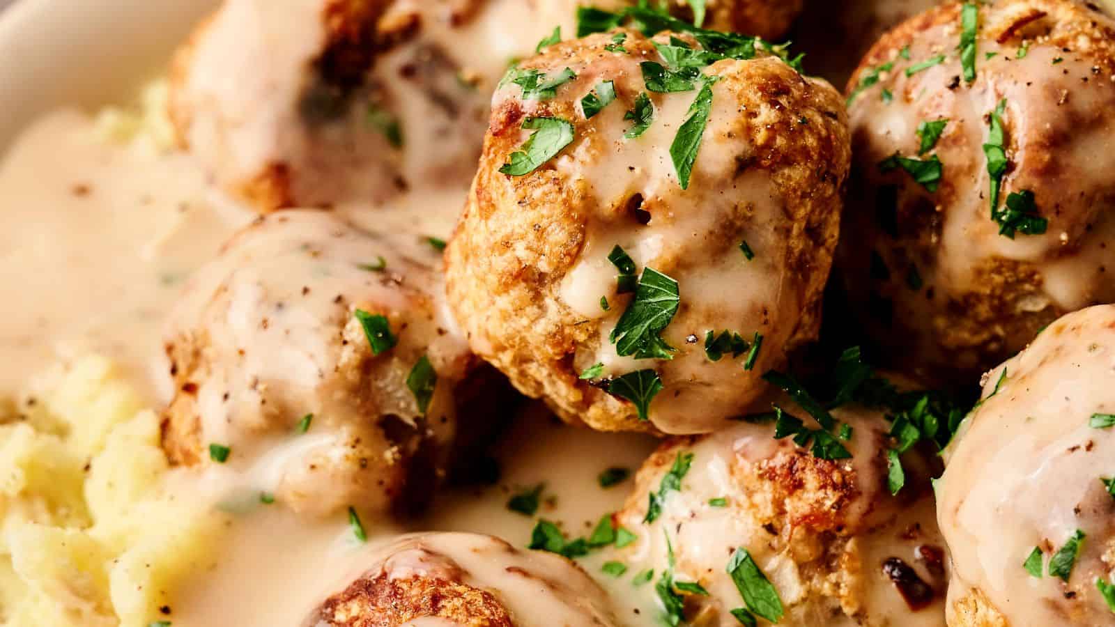 Close-up of meatballs covered in gravy, topped with chopped parsley, resting on mashed potatoes.