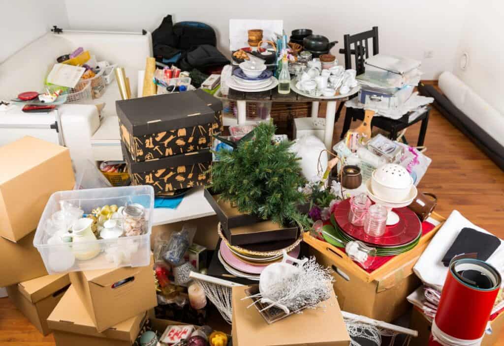 A cluttered room filled with doom boxes, household items, and a small artificial tree on a wooden floor.