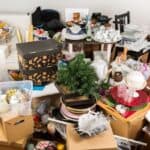 A cluttered room filled with doom boxes, household items, and a small artificial tree on a wooden floor.