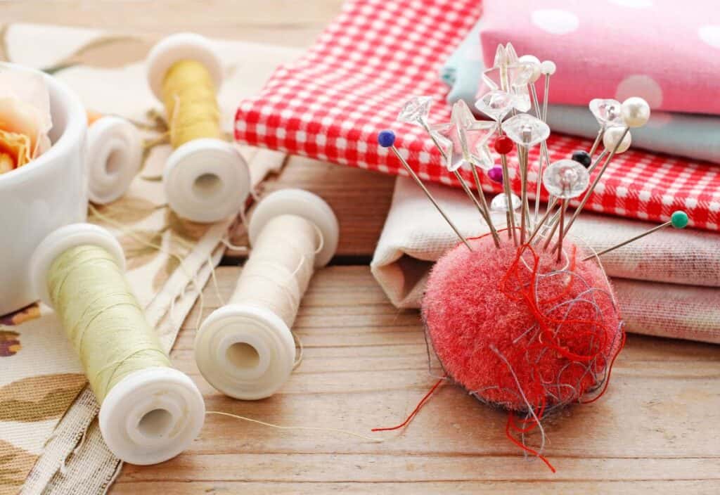 Sewing supplies including colorful fabric, a pincushion with pins, and spools of thread on a wooden surface celebrate the timeless art of old skills.