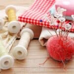 Sewing supplies including colorful fabric, a pincushion with pins, and spools of thread on a wooden surface celebrate the timeless art of old skills.