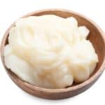 A wooden bowl filled with white lard on a white background.