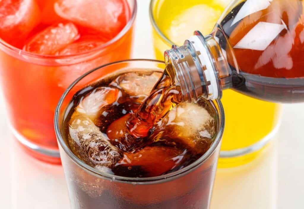 Pouring cola into a glass with ice, surrounded by red and yellow drinks.