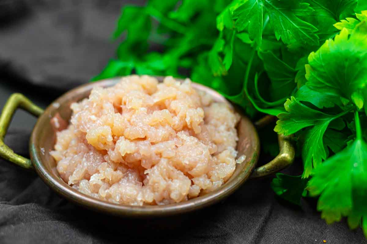 A bowl of minced meat with fresh green parsley leaves beside it.