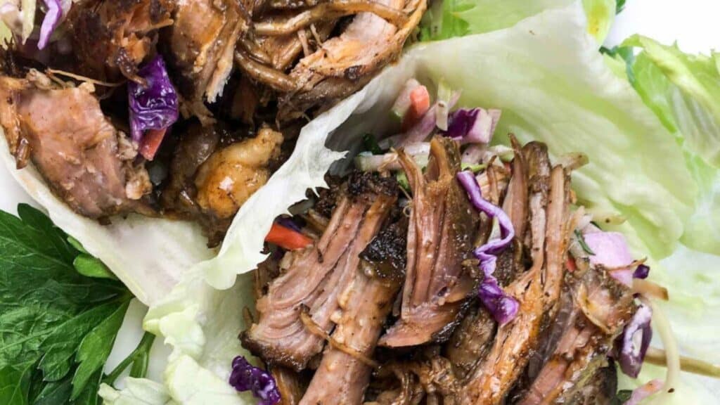 Shredded meat and purple cabbage served on lettuce leaves, garnished with herbs.