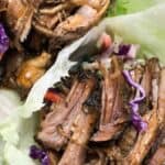 Shredded meat and purple cabbage served on lettuce leaves, garnished with herbs.