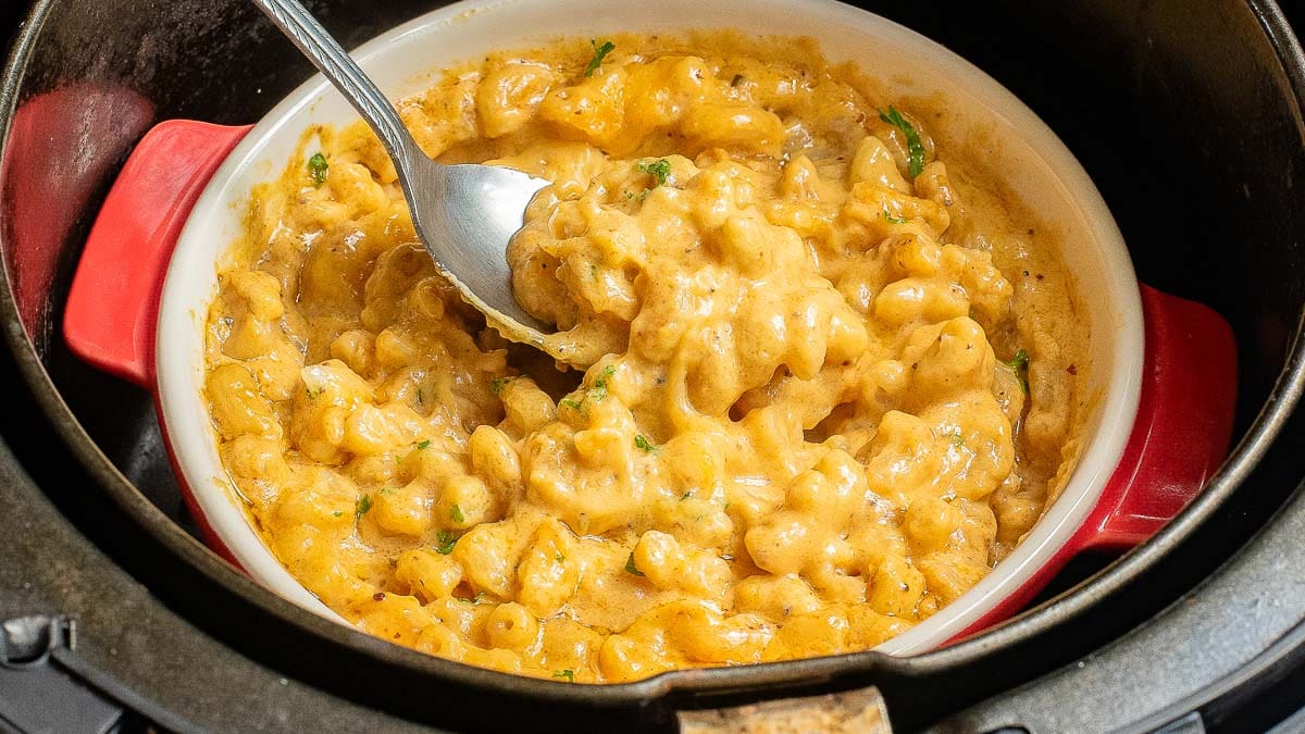 A bowl of creamy macaroni and cheese with a spoon, inside an air fryer.