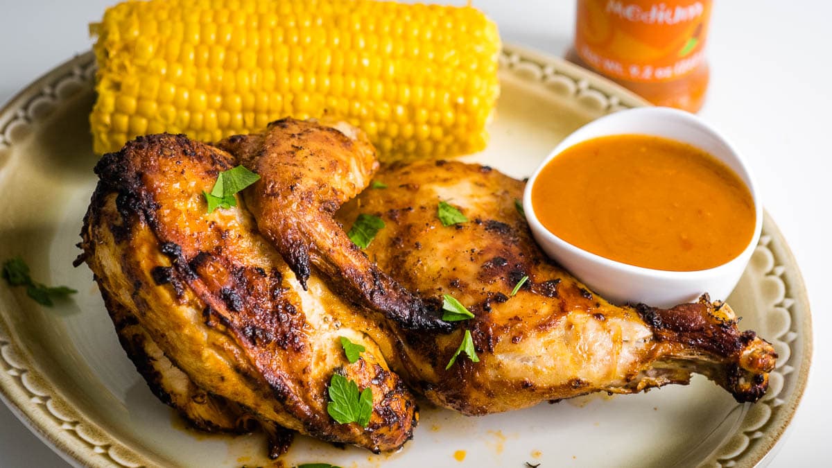 Grilled chicken pieces with sauce, garnished with parsley, served on a plate with a corn on the cob.