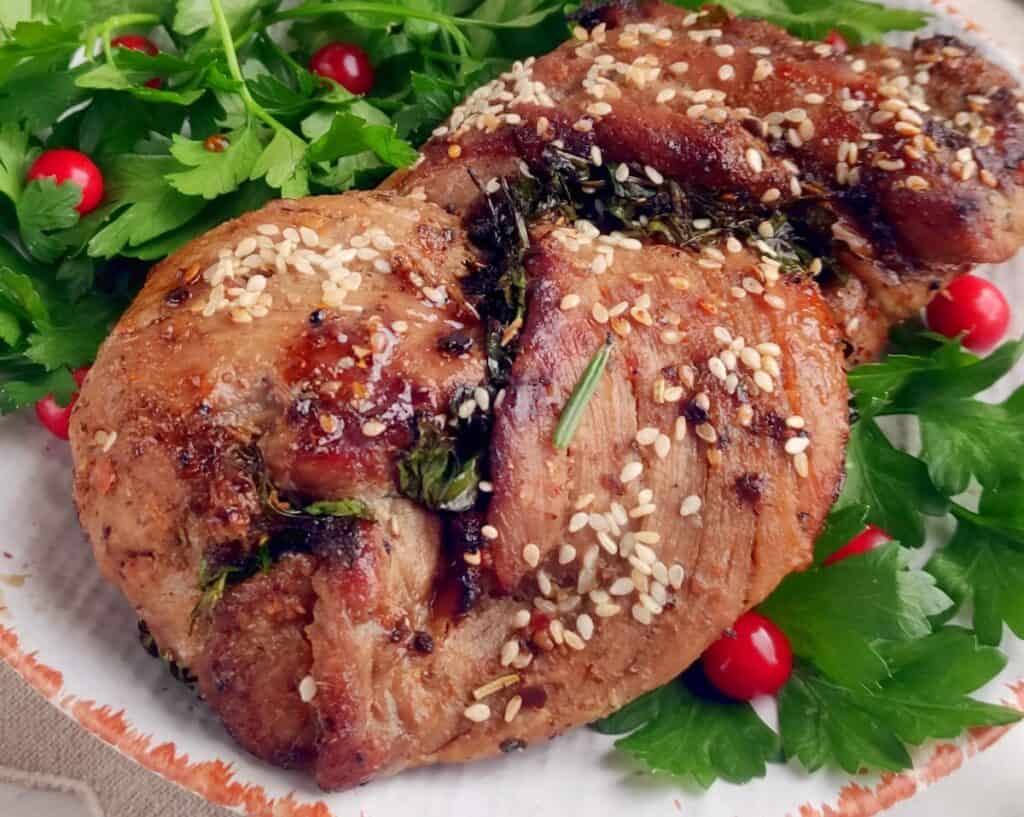 Grilled meat garnished with sesame seeds and herbs, served on a plate with fresh parsley and red berries.