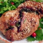 Grilled meat garnished with sesame seeds and herbs, served on a plate with fresh parsley and red berries.