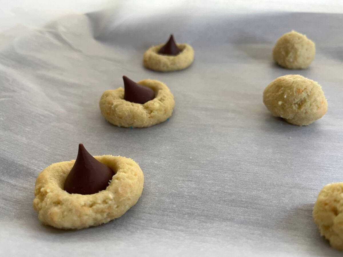 Unbaked cookies on parchment paper, some topped with chocolate pieces and others in ball shapes.