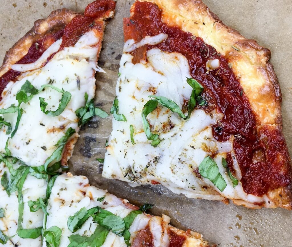 Close-up of two slices of pizza with cheese, tomato sauce, and fresh basil on parchment paper.