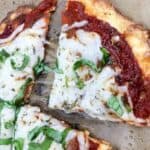 Close-up of two slices of pizza with cheese, tomato sauce, and fresh basil on parchment paper.