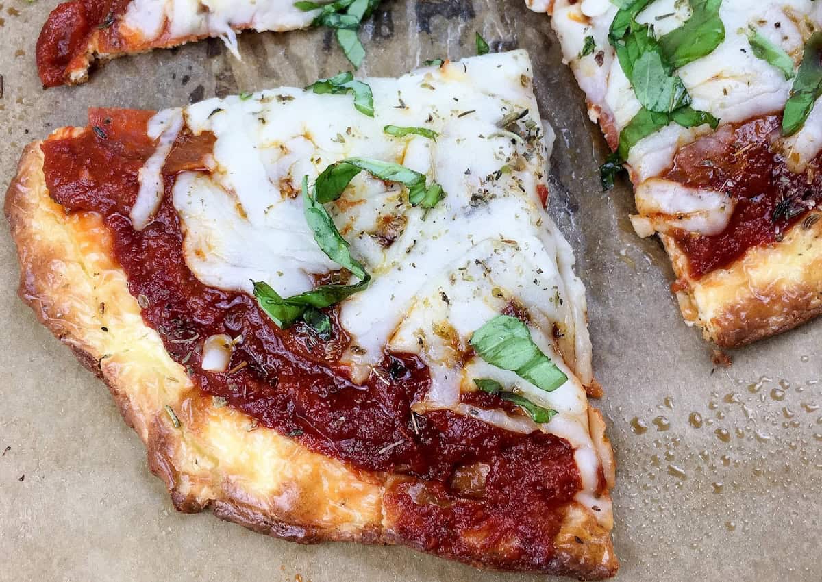 Close-up of a cheese pizza slice with tomato sauce and fresh basil on a parchment background.