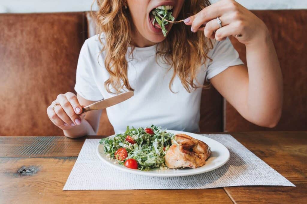 Enjoying a fresh salad with cherry tomatoes and chicken at a wooden table, this moment feels as delightful as receiving the perfect 21st birthday gift.