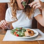 Enjoying a fresh salad with cherry tomatoes and chicken at a wooden table, this moment feels as delightful as receiving the perfect 21st birthday gift.