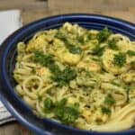 A plate of linguine with shrimp and pesto sauce, garnished with parsley. A fork and napkin are placed beside the dish.